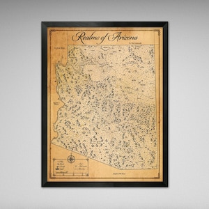 May include: Framed map print titled "Realms of Arizona." The map features detailed illustrations of the state's topography, with a compass rose and legend in the lower left corner. The map is printed on aged paper and framed in a black frame.