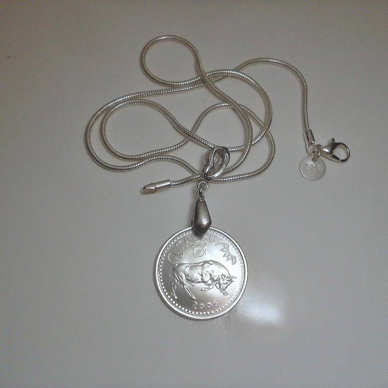 May include: A silver-colored snake chain necklace featuring a round pendant with a bull illustration, the text TAURUS, and the year 2008. The pendant is attached to a silver bail, and the chain includes a lobster clasp with a small round 925 tag.