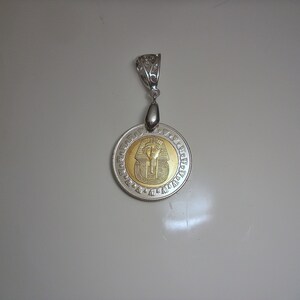 Op de afbeelding: Een zilveren hanger met een rond gouden sieraad met een buste van een Egyptische farao. De hanger is omringd door hi&euml;rogliefen.