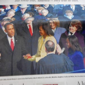 May include: A photograph of a presidential inauguration ceremony. The central figure, wearing a dark suit and red tie, raises his right hand. Other figures in formal attire are present, with a crowd in the background.