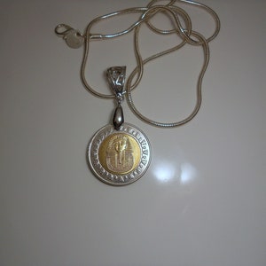 Op de afbeelding: Een zilveren ketting met een ronde hanger met een gouden Egyptisch faraosymbool.