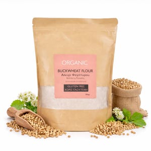 Può includere: Un sacchetto di carta marrone di farina di grano saraceno biologica con un'etichetta rosa. L'etichetta recita "Organic Buckwheat Flour" in inglese e greco, con "Gluten Free" sotto. Grani di grano saraceno e un cucchiaio di legno circondano il sacchetto.