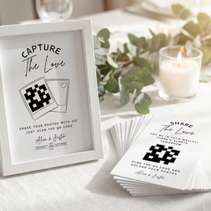 Puede incluir: Un letrero enmarcado en blanco con el texto "CAPTURE The Love" y un código QR. Junto a él, una pila de tarjetas con el texto "SHARE The Love" y un código QR. Una vela encendida y vegetación en el fondo.