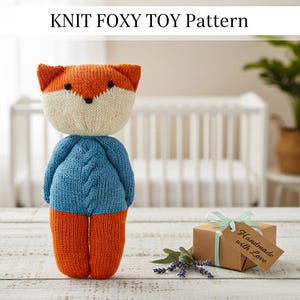 May include: A knitted fox toy with orange, cream, and blue colors. The fox has orange ears and legs, a cream-colored head, and a blue sweater. The text "KNIT FOXY TOY Pattern" is at the top of the image. A small gift box with a tag that says "Handmade with Love" is also in the image.