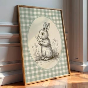 May include: A framed print with a detailed sketch of a rabbit holding flowers. The artwork is set against a light green and white gingham pattern, framed in wood. The overall aesthetic is vintage and evokes a sense of spring.
