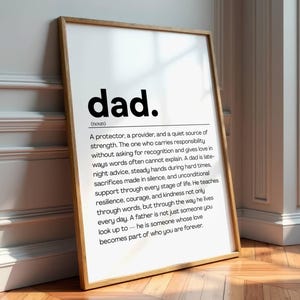 Op de afbeelding: Een ingelijste print met een houten frame, leunend tegen een muur. De print bevat het woord "dad" in vette zwarte letters, gevolgd door een definitie. De definitie beschrijft de rol van een vader in een gezin.