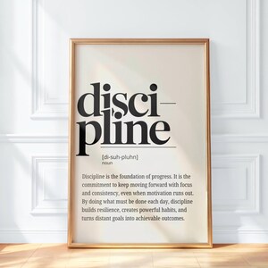 May include: A framed print with the word "discipline" in large, bold, black letters. The definition of discipline is below the word, in a smaller font. The frame is a light gold color.