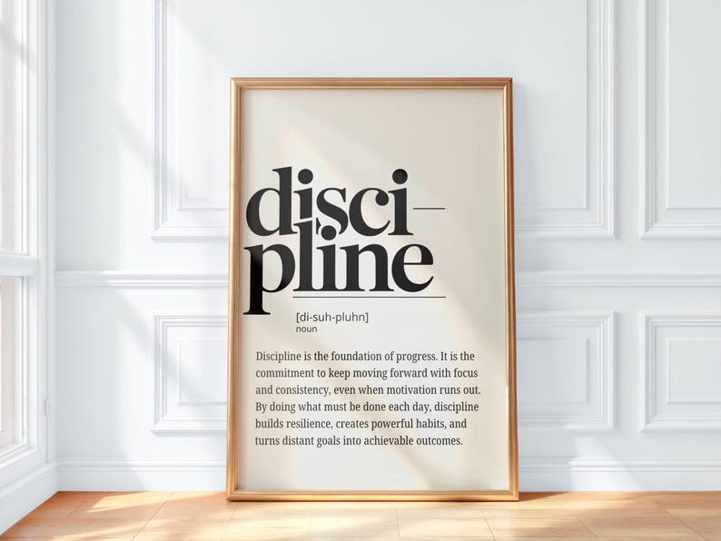 May include: A framed print with the word "discipline" in large, bold, black letters. The definition of discipline is below the word, in a smaller font. The frame is a light gold color.
