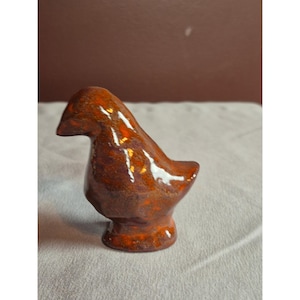 May include: A ceramic bird figurine in shades of brown and orange. The bird has a rounded body, a small beak, and a glossy finish. The figurine is a decorative item, likely for display.