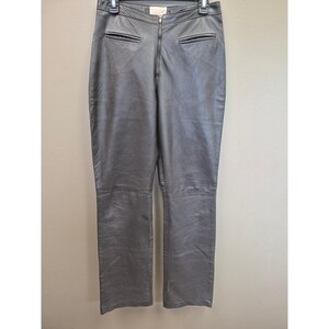 May include: Gray leather pants with a zipper fly and two front pockets. The pants are hanging on a hanger against a neutral background. The leather has a slight sheen.