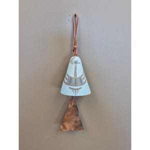 May include: A light blue ceramic bell with a brown leather strap. The bell has a painted design in white and blue. A copper-colored triangle hangs below the bell.