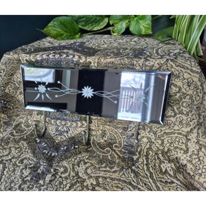 May include: A rectangular, mirrored wall hook with three metal hooks. The mirror has a floral design etched across the surface. The hooks are silver-toned and attached to the bottom of the mirror.