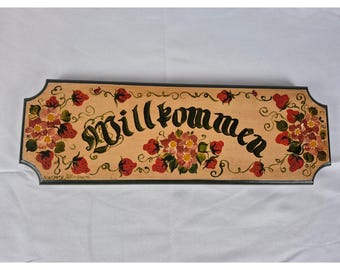 Letrero de pared de madera vintage pintado a mano con la inscripción "Willkommen" (Bienvenido/a) y diseño floral de fresas.