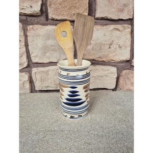 May include: A white ceramic mug with a black handle and the text "But First, Coffee" in a black, handwritten-style font. The mug is on a white surface.