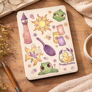 May include: Cream-colored tablet case featuring colorful illustrations of a tower, sun, flowers, a frog, and a duck with the text "The Snuggly Duckling." The case has a whimsical, cartoon-like design.