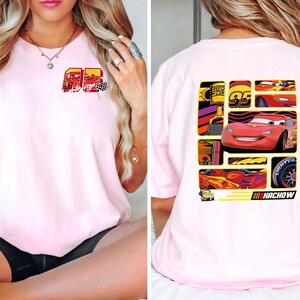 May include: Light pink t-shirt featuring a graphic of a red race car and the number 95. The front of the shirt has a smaller graphic with the number 95 and a checkered flag. The back of the shirt has a larger graphic with the race car and the word "Kachow".