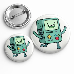 May include: Three round buttons with a cartoon design of a teal video game console character with arms and legs. The character has a smiling face and the letters "BM" on the side. One button is a pin back.