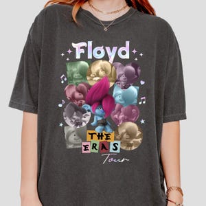 Könnte beinhalten: Dunkelgraues T-Shirt mit einer farbenfrohen Grafik der Figur Floyd aus dem Film Trolls. Das Design enthält den Text "Floyd" in einer holografischen Schriftart sowie die Worte "The Eras Tour". Das Shirt hat einen Vintage-Look.