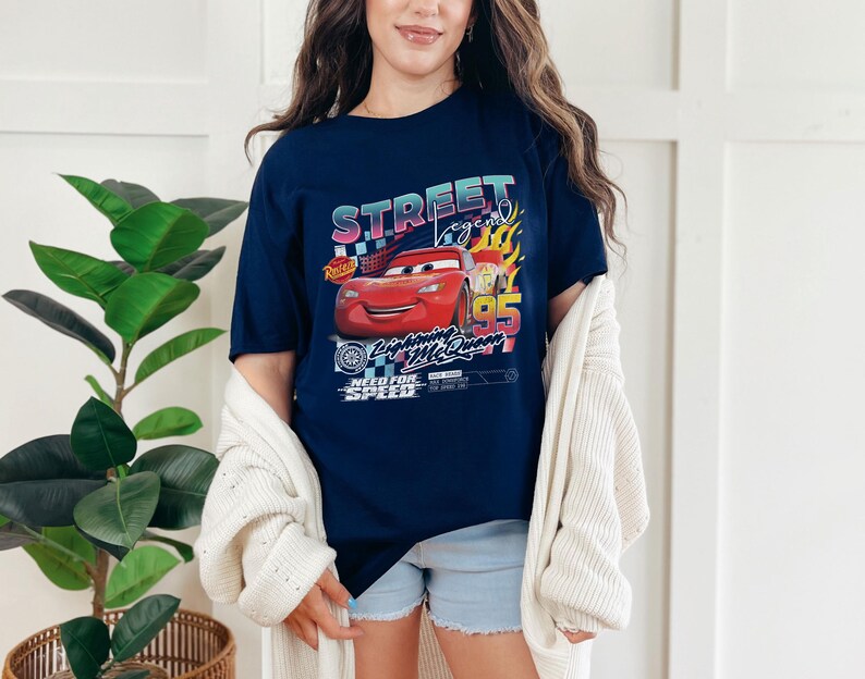 May include: Navy blue t-shirt featuring a graphic of Lightning McQueen from the movie Cars. The design includes the text "Street Legend" and "Lightning McQueen 95" with racing-themed elements. The shirt is worn by a person.