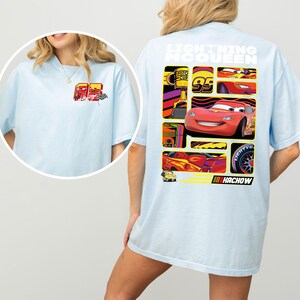 May include: Light blue t-shirt featuring a graphic of Lightning McQueen from the movie Cars. The back of the shirt displays a collage of images of the character and the text "Lightning McQueen" and "Hachow". The front of the shirt has a smaller graphic of the character.