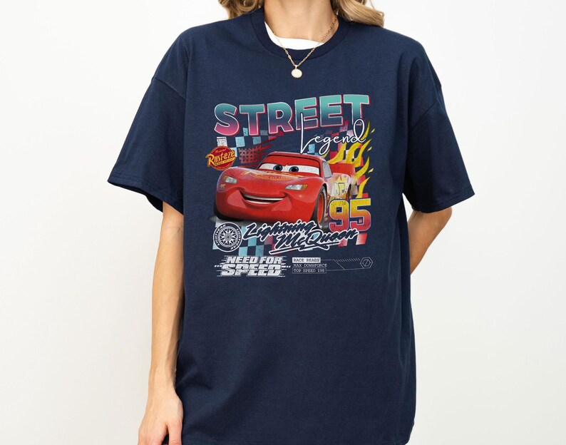 May include: Navy blue t-shirt featuring a graphic of Lightning McQueen from the movie Cars. The design includes the text "STREET LEGEND", "Lightning McQueen 95", and "NEED FOR SPEED". The graphic has a colorful, retro style.