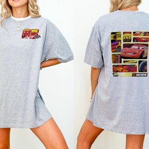 May include: A light gray t-shirt featuring a graphic of the character Lightning McQueen from the movie Cars. The front of the shirt has the number 95 and a checkered flag. The back of the shirt has a collage of images of Lightning McQueen.
