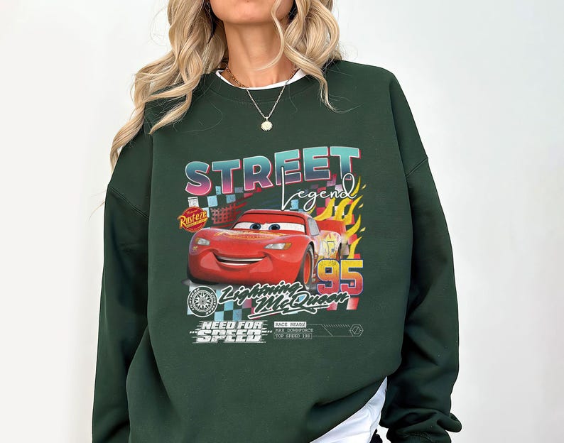 May include: Dark green sweatshirt featuring a graphic of Lightning McQueen from the movie Cars. The design includes the text "Street Legend", "Lightning McQueen", and "Need for Speed". The number "95" is also prominently displayed.