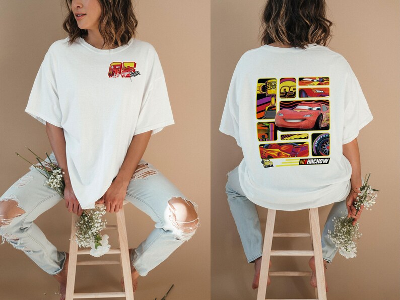 May include: White t-shirt featuring a colorful graphic of a race car on the back and a smaller design on the front. The back graphic includes the text "NACHOW". The shirt is worn with ripped blue jeans.