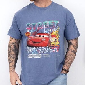 May include: Blue t-shirt featuring a graphic of Lightning McQueen from the movie Cars. The design includes the text "STREET legend" and "95", with flames and other design elements. The shirt has a crew neck and short sleeves.