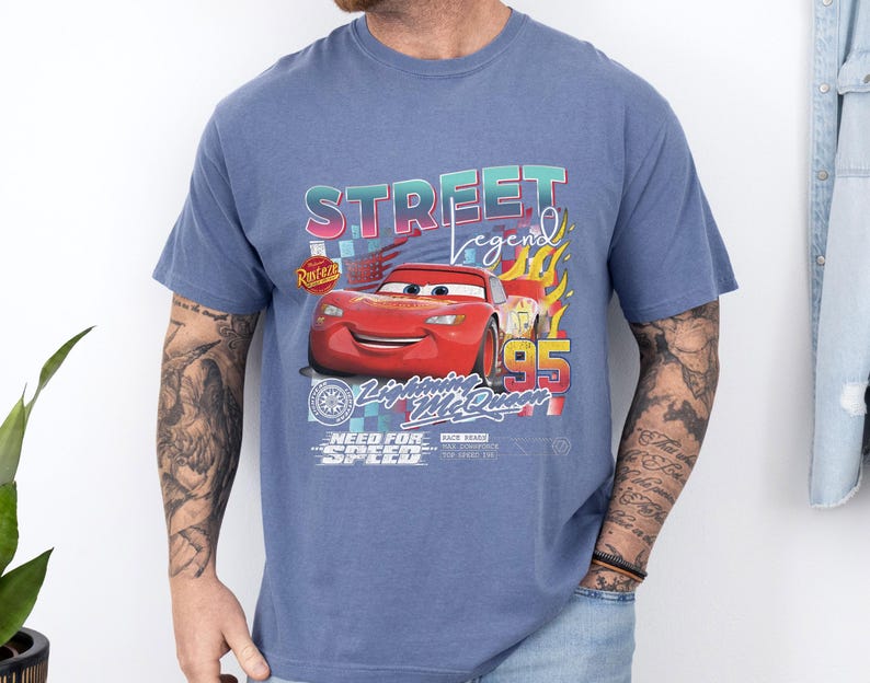 May include: Blue t-shirt featuring a graphic of Lightning McQueen from the movie Cars. The design includes the text "STREET legend" and "95", with flames and other design elements. The shirt has a crew neck and short sleeves.