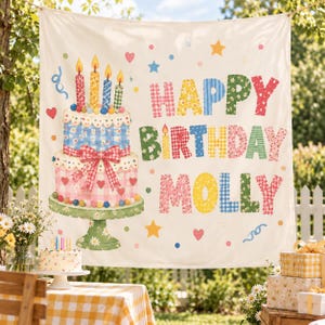 May include: A white fabric banner featuring a two-tiered birthday cake illustration with a red gingham bow, four lit candles, and the text HAPPY BIRTHDAY MOLLY in colorful patterned letters, accented by small hearts, stars, and confetti dots.