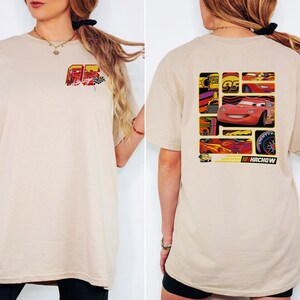 May include: Beige t-shirt featuring a graphic of a race car on the back and a smaller design on the front. The back design includes the number 95, a tire, and the word "HACHOW". The front design includes the number 95 and a checkered flag.