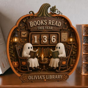 May include: A pumpkin-shaped wooden display featuring two white ghost figurines sitting in rocking chairs and reading books. The display includes a flip-style counter showing 136, text reading BOOKS READ THIS YEAR and OLIVIA'S LIBRARY, and miniature lanterns.