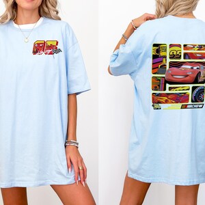 May include: Light blue t-shirt featuring a graphic of a red race car with the number 95 and the word "HACHOW". The front of the shirt has a smaller graphic with the number 95 and a checkered flag. The shirt has short sleeves and a relaxed fit.