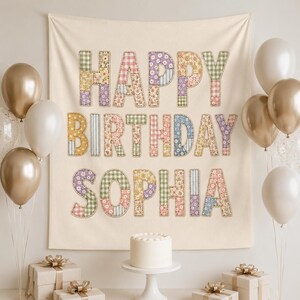 May include: A cream-colored fabric backdrop featuring the text HAPPY BIRTHDAY SOPHIA in large, block letters. Each letter is filled with a patchwork of various floral, gingham, and striped patterns in pastel shades of pink, blue, yellow, and green.