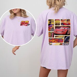 May include: A light purple t-shirt featuring a graphic of a red race car and the number 95. The back of the shirt has a larger design with the race car and other racing-themed graphics. The word "HACHOW" is printed at the bottom.