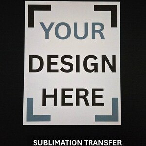 May include: A white rectangular sublimation transfer with the words "YOUR DESIGN HERE" in black and grey lettering. The text is framed by black and grey corner brackets. The bottom of the transfer reads "SUBMLIMATION TRANSFER NO SHIRT INCLUDED".
