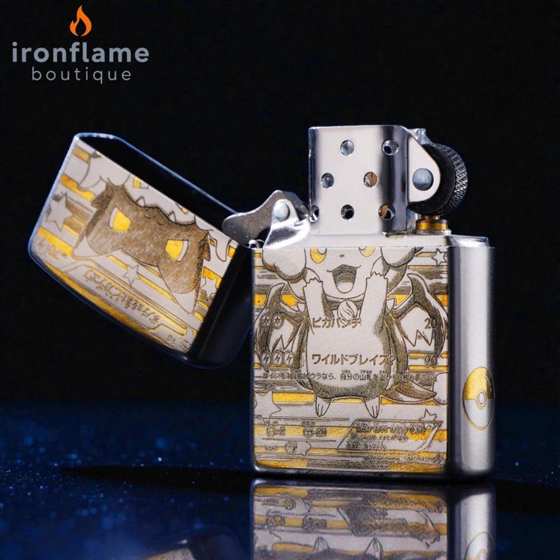 May include: A silver metal lighter with a hinged lid, featuring a detailed illustration of a cartoon character with Japanese text. The lighter is open, revealing the interior design. The text "ironflame boutique" is at the top.