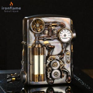 Peut inclure: Un briquet de style steampunk avec des engrenages complexes, des jauges et des accents m&eacute;talliques. Le briquet pr&eacute;sente une combinaison de tons bronze, argent et or, avec une petite jauge et un &eacute;l&eacute;ment en forme d'&eacute;ventail. La marque "ironflame boutique" est visible.
