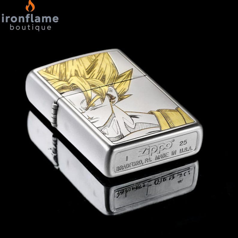 May include: A silver Zippo lighter with a detailed engraving of a character with spiky yellow hair. The lighter has a brushed metal finish and the text "Zippo" and "BRADFORD, PA. MADE IN U.S.A." are visible.