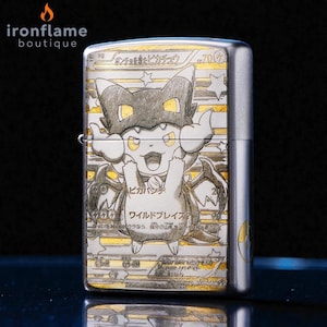 May include: A silver metal lighter featuring a detailed illustration of a Pikachu character in a costume. The design includes Japanese text and star accents. The lighter has a hinged lid and a side lever.