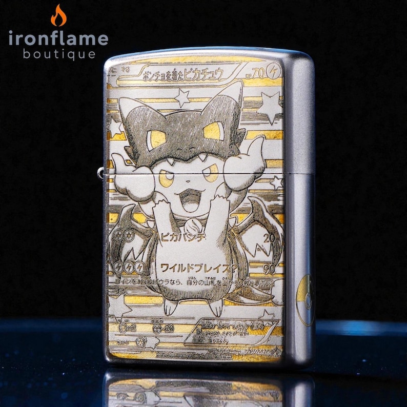 May include: A silver metal lighter featuring a detailed illustration of a Pikachu character in a costume. The design includes Japanese text and star accents. The lighter has a hinged lid and a side lever.