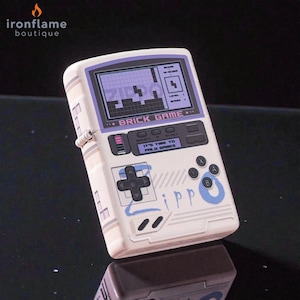 May include: A white lighter with a retro video game design. The screen shows a Tetris-style game with the text "BRICK GAME." It has a directional pad, buttons, and the text "IT'S TIME TO PLAY GAMES."