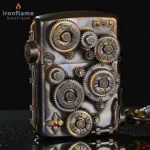 Peut inclure: Un briquet de style steampunk avec une finition m&eacute;tallique, orn&eacute; de motifs d'engrenages complexes dans des tons argent et or. Le briquet pr&eacute;sente un couvercle &agrave; charni&egrave;re et une esth&eacute;tique m&eacute;canique d&eacute;taill&eacute;e, avec le logo "ironflame boutique".