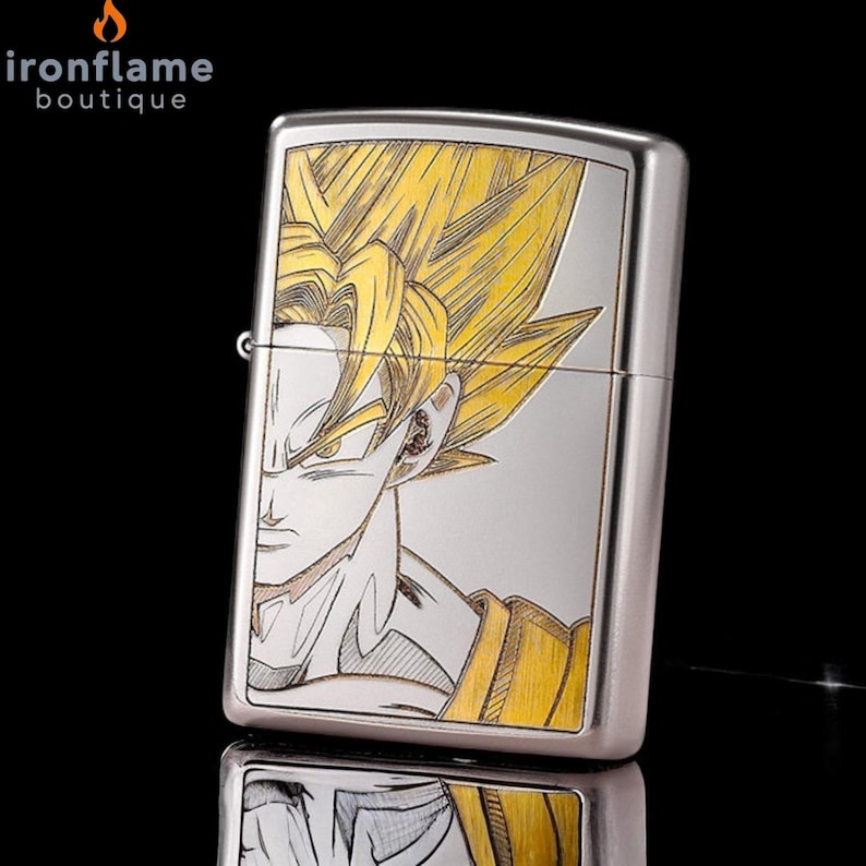 May include: A silver-colored lighter featuring a detailed illustration of a character with spiky yellow hair and a determined expression. The character is wearing a yellow and orange outfit. The lighter has a rectangular shape.