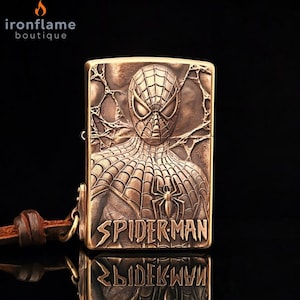 May include: A bronze-coloured lighter with an embossed Spider-Man design. The lighter has the words "SPIDER-MAN" in a bold font and a leather strap. The brand name "ironflame boutique" is in the top left corner.