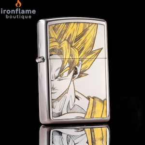 May include: A silver-colored lighter featuring a detailed illustration of a character with spiky yellow hair and a determined expression. The artwork is set against a white background, with yellow and black accents. The lighter has a reflective surface.