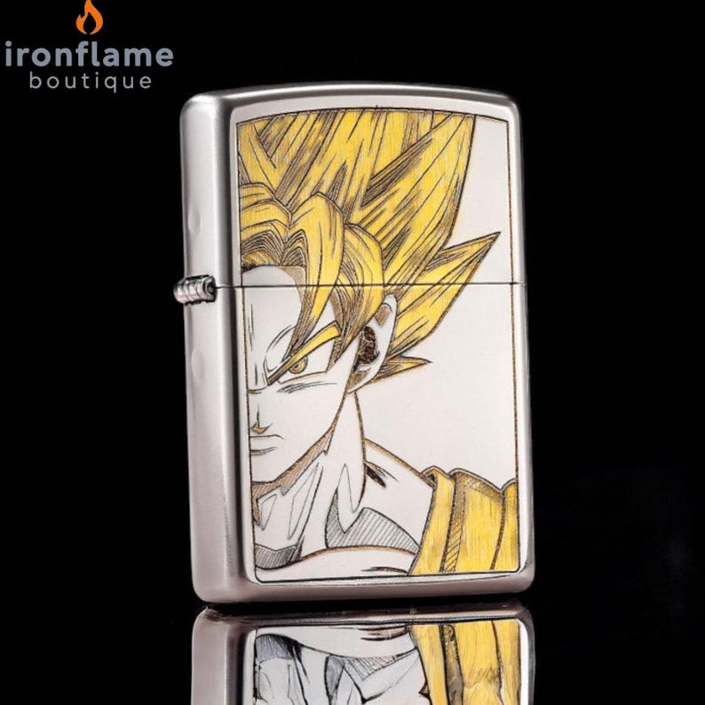 May include: A silver-colored lighter featuring a detailed illustration of a character with spiky yellow hair and a determined expression. The artwork is set against a white background, with yellow and black accents. The lighter has a reflective surface.