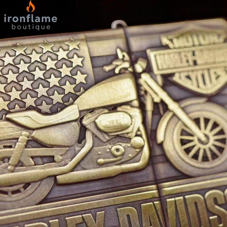Pu&ograve; includere: Un emblema dettagliato di motocicletta Harley-Davidson color bronzo con un design a bandiera americana. L'emblema presenta una motocicletta, stelle e il logo Harley-Davidson. Il logo della boutique Ironflame si trova nell'angolo in alto a sinistra.