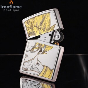 May include: A silver metal lighter with a hinged lid, featuring a detailed illustration of a character with yellow hair and a determined expression. The lighter is open, revealing its internal components. The brand name "ironflame boutique" is visible.